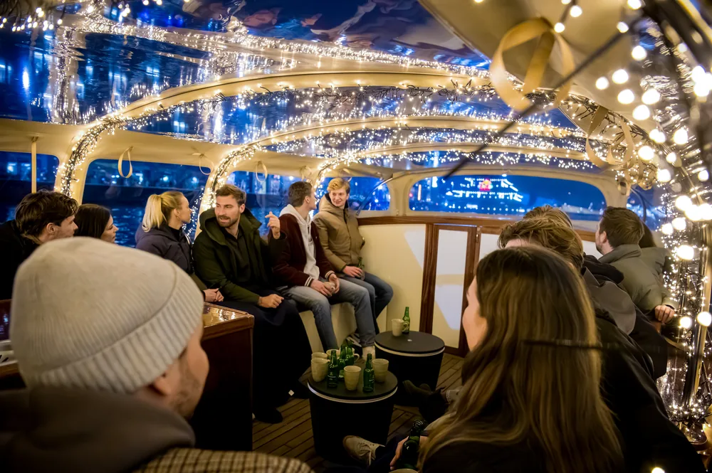 Gasten aan boord van de sloep met gesloten overkapping tijdens een winteravond op de Amsterdamse grachten